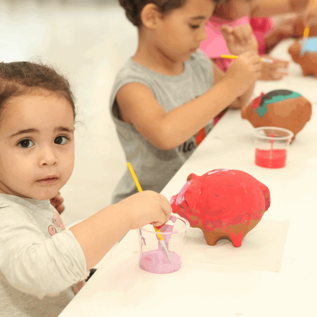 Criança pintando e montando bolsinhas em cima de uma mesa branca